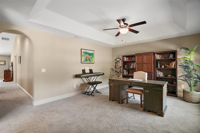 home office featuring arched walkways, a raised ceiling, ceiling fan, and light carpet