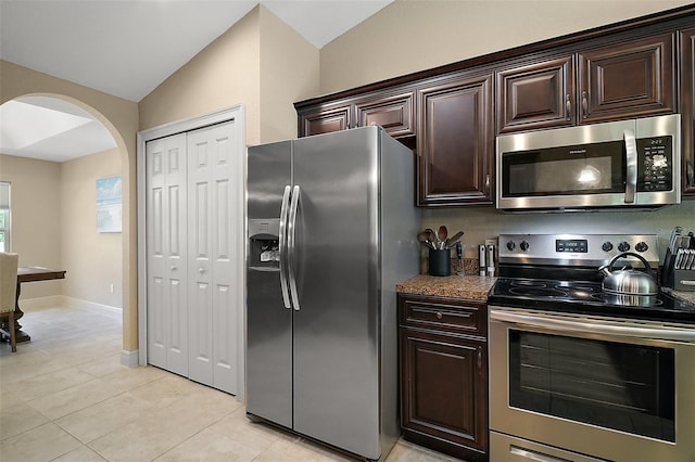 kitchen featuring dark brown cabinetry, appliances with stainless steel finishes, arched walkways, light tile patterned floors, and lofted ceiling