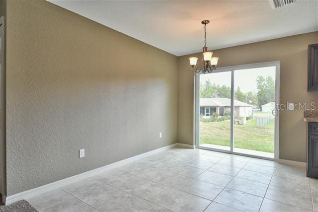 spare room with baseboards, a textured wall, light tile patterned floors, and a notable chandelier