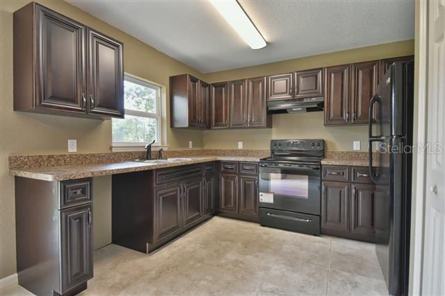 kitchen featuring a sink, dark brown cabinets, black appliances, and under cabinet range hood