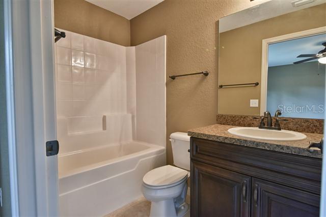 full bathroom with vanity, a textured wall, toilet, bathtub / shower combination, and a ceiling fan