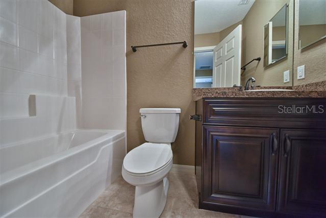 bathroom with toilet, a textured wall, shower / tub combination, and vanity