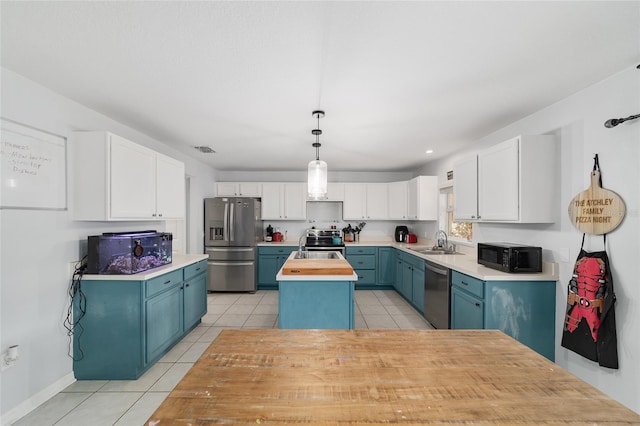 kitchen featuring appliances with stainless steel finishes, a sink, a kitchen island with sink, light tile patterned floors, and blue cabinets