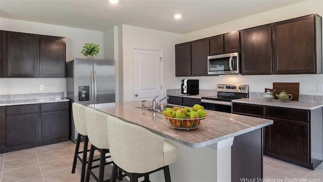 kitchen with dark brown cabinetry, appliances with stainless steel finishes, a breakfast bar, a sink, and light tile patterned floors