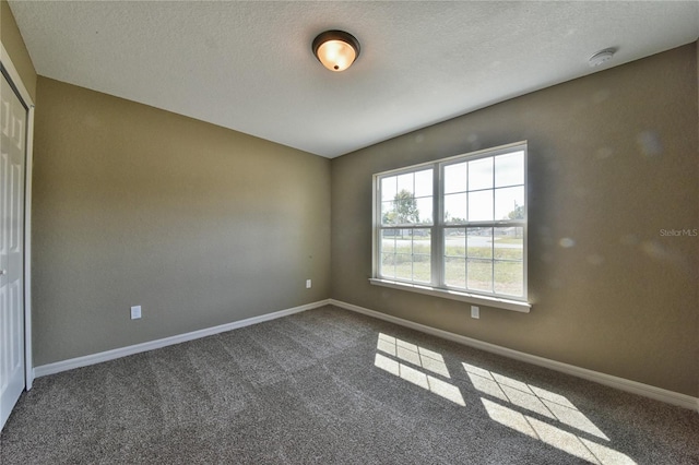 empty room featuring a textured ceiling, baseboards, and dark carpet