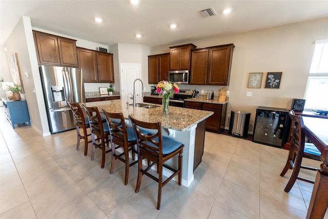 kitchen featuring visible vents, light stone countertops, a center island with sink, a sink, and appliances with stainless steel finishes
