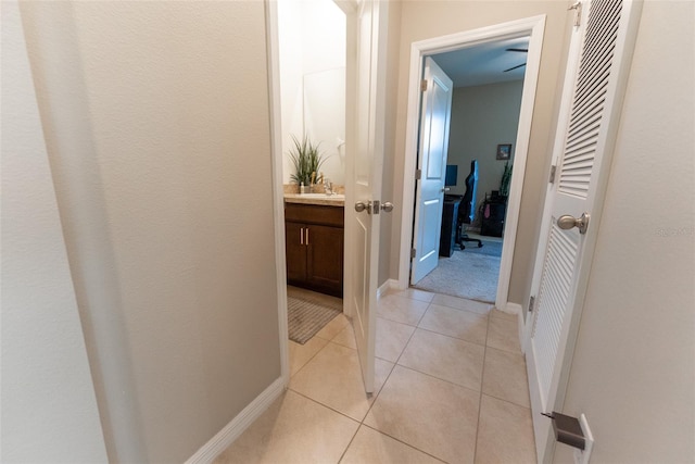 hallway featuring baseboards, a sink, and light tile patterned flooring