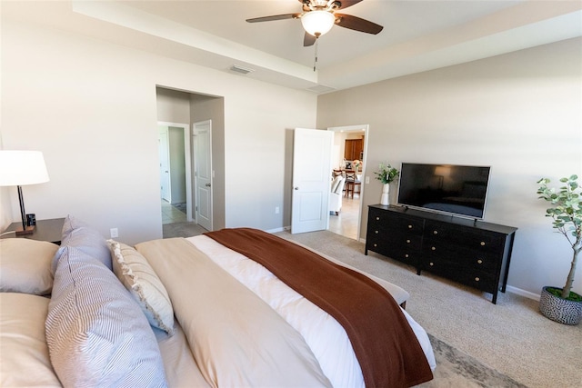 bedroom with ceiling fan, light colored carpet, visible vents, a raised ceiling, and baseboards
