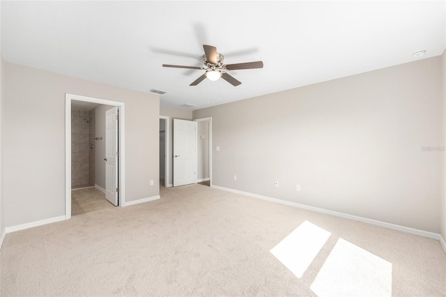 unfurnished bedroom featuring light colored carpet, baseboards, a ceiling fan, ensuite bathroom, and a walk in closet