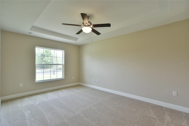spare room with baseboards, ceiling fan, a tray ceiling, and light colored carpet