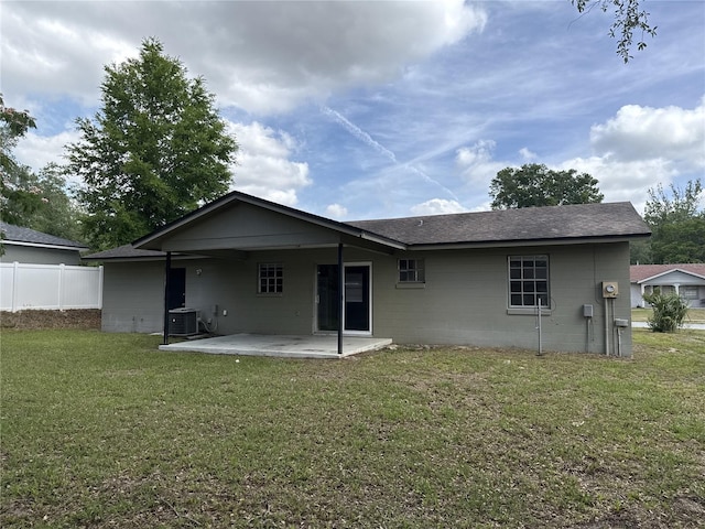 rear view of house featuring fence, a shingled roof, concrete block siding, a patio, and a yard
