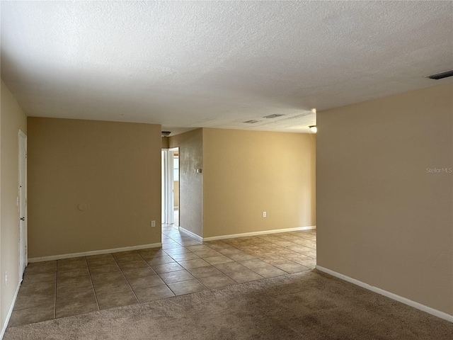 carpeted spare room featuring tile patterned flooring, a textured ceiling, baseboards, and visible vents