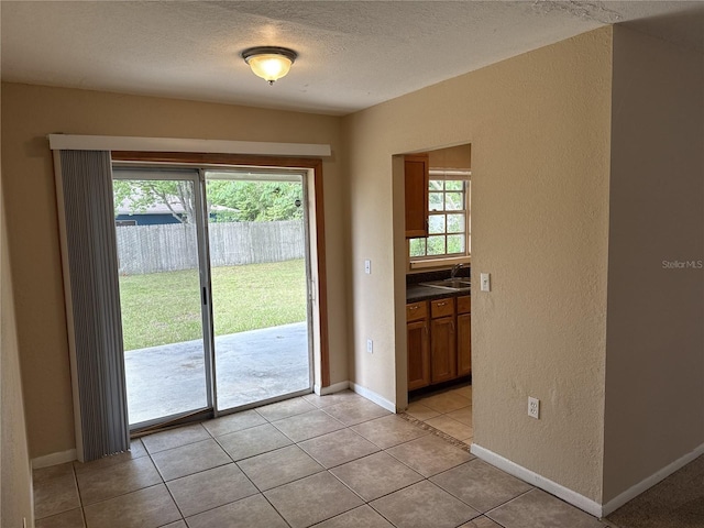 doorway with a textured wall, light tile patterned flooring, baseboards, a textured ceiling, and a sink