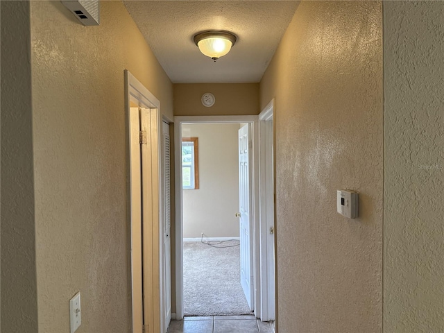 corridor with a textured ceiling, a textured wall, and tile patterned floors