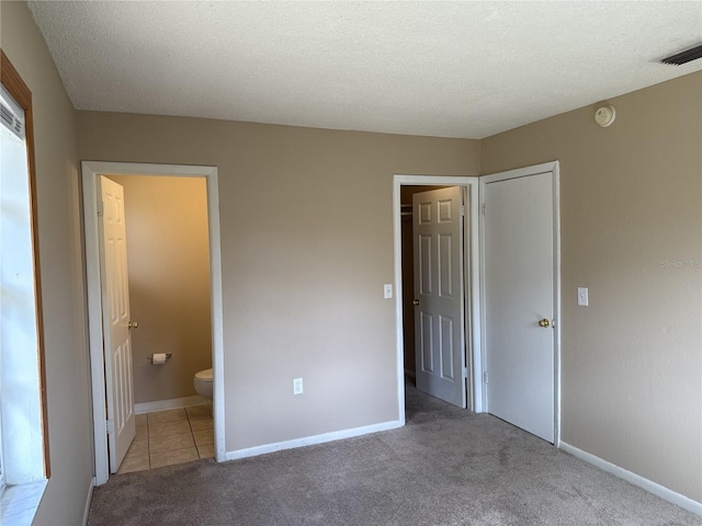 unfurnished bedroom with baseboards, visible vents, ensuite bathroom, and light colored carpet