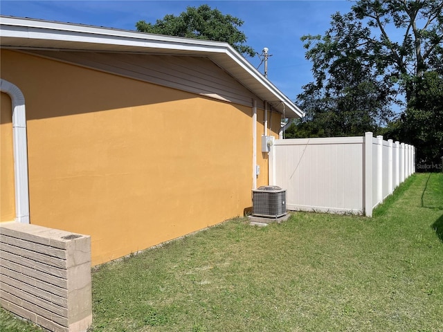 view of side of property featuring a lawn, central AC, stucco siding, and fence