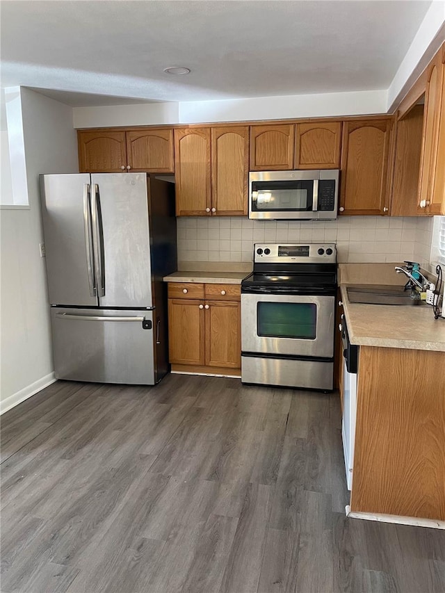 kitchen with appliances with stainless steel finishes, dark wood-style floors, a sink, and tasteful backsplash