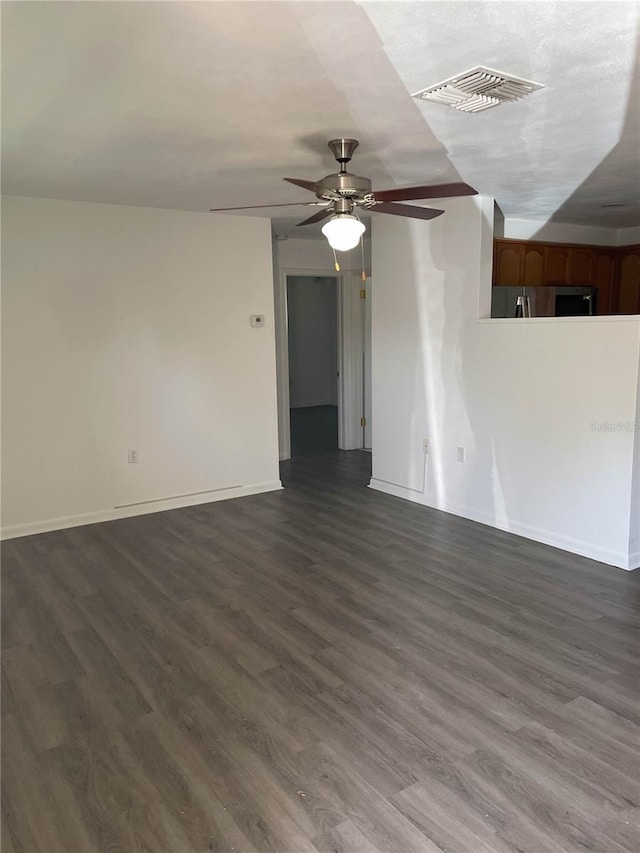 spare room with visible vents, a ceiling fan, dark wood finished floors, and baseboards