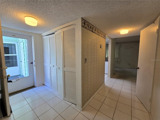 hall featuring baseboards, a textured ceiling, and light tile patterned floors