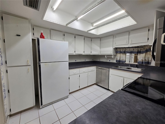 kitchen featuring light tile patterned flooring, dark countertops, a sink, dishwasher, and freestanding refrigerator