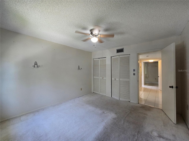 unfurnished bedroom with visible vents, multiple closets, light colored carpet, a textured ceiling, and a ceiling fan