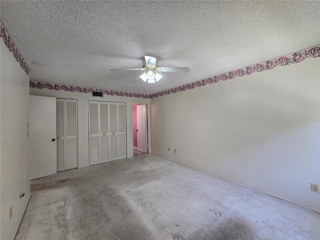 unfurnished bedroom featuring visible vents, a textured ceiling, ceiling fan, and two closets