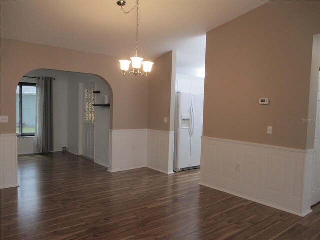 spare room with arched walkways, a chandelier, dark wood finished floors, and a wainscoted wall