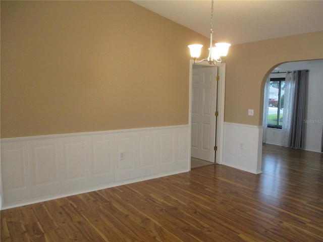 unfurnished room featuring an inviting chandelier, arched walkways, wainscoting, and dark wood finished floors