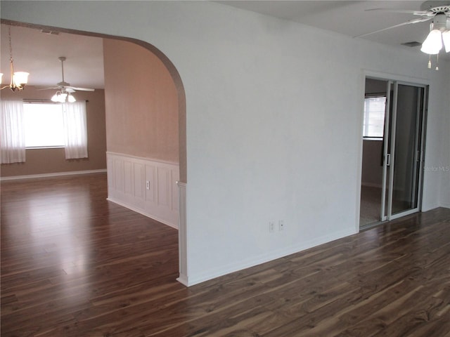 spare room featuring dark wood-type flooring, arched walkways, wainscoting, and ceiling fan with notable chandelier