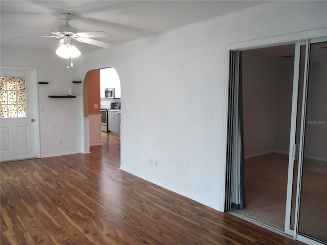 interior space featuring arched walkways, ceiling fan, dark wood finished floors, and baseboards
