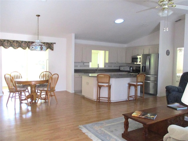 interior space with dark countertops, appliances with stainless steel finishes, a kitchen breakfast bar, a kitchen island, and vaulted ceiling