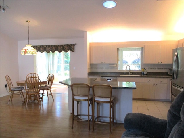 kitchen featuring dark countertops, a sink, a breakfast bar area, stainless steel appliances, and decorative light fixtures