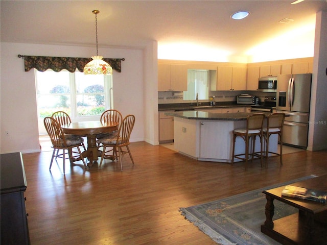 kitchen with dark countertops, a breakfast bar area, stainless steel appliances, wood finished floors, and a kitchen island