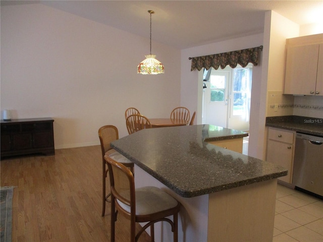 kitchen with hanging light fixtures, a kitchen breakfast bar, lofted ceiling, stainless steel dishwasher, and a kitchen island