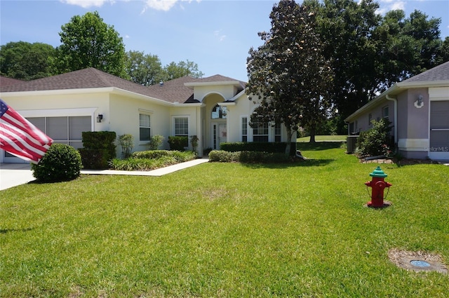 view of front of property featuring roof with shingles, an attached garage, stucco siding, a front yard, and central AC unit