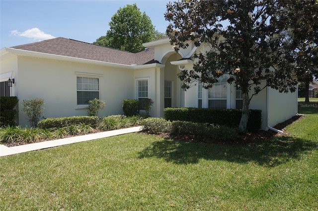 view of front of house with stucco siding, a shingled roof, and a front lawn