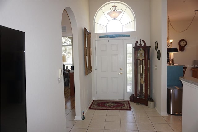 foyer entrance featuring baseboards, visible vents, light tile patterned floors, and a high ceiling