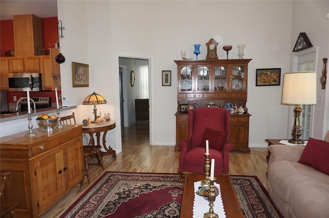 living room with a high ceiling, baseboards, and light wood-type flooring