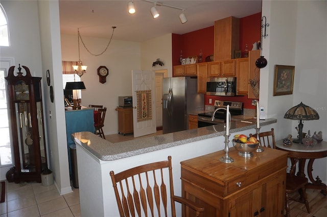 kitchen with a peninsula, light tile patterned flooring, brown cabinets, rail lighting, and stainless steel appliances