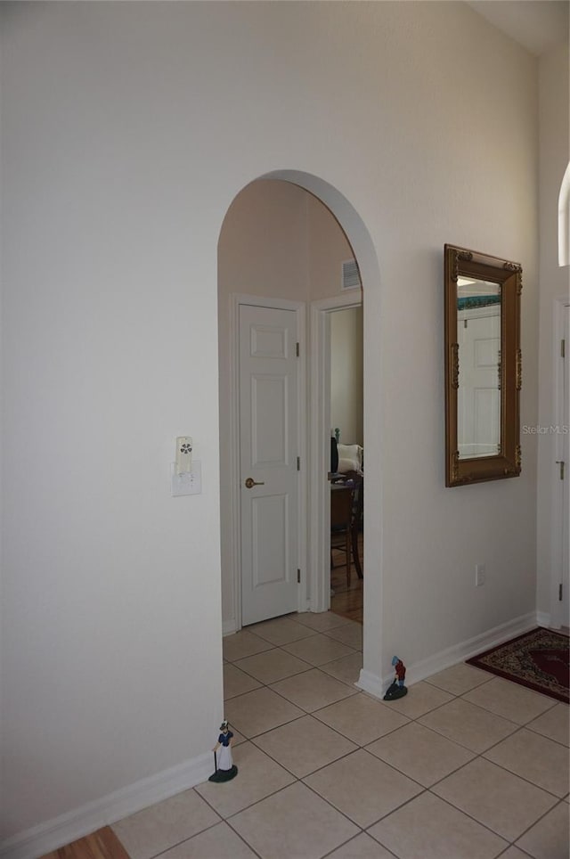 hall featuring light tile patterned floors, arched walkways, baseboards, and visible vents