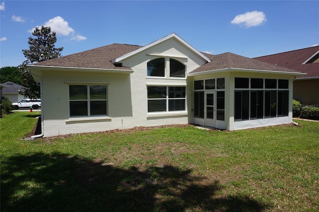 back of house with roof with shingles, a yard, stucco siding, and a sunroom