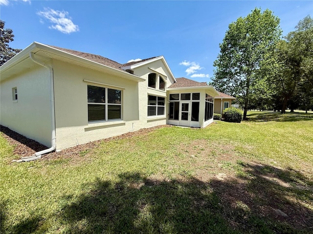 rear view of property with a shingled roof, a yard, stucco siding, and a sunroom