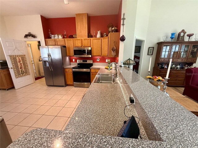 kitchen with brown cabinetry, a high ceiling, a sink, appliances with stainless steel finishes, and light tile patterned floors