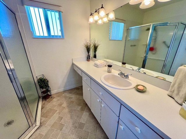 bathroom with a stall shower, vanity, baseboards, and stone finish flooring