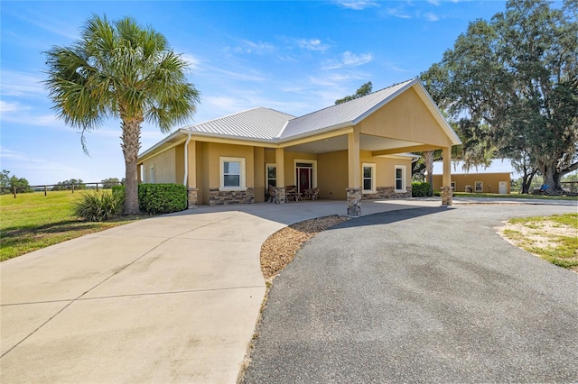view of front of home featuring stucco siding, driveway, stone siding, and metal roof