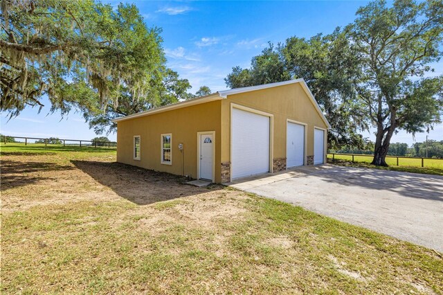 view of side of property featuring a garage, fence, stucco siding, an outbuilding, and a yard