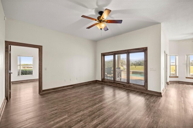 unfurnished living room featuring plenty of natural light, a ceiling fan, baseboards, and dark wood-style floors