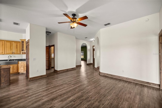 unfurnished living room featuring visible vents, arched walkways, dark wood-style flooring, and ceiling fan