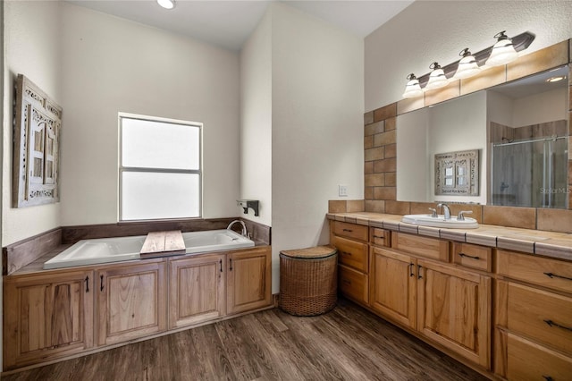 bathroom featuring backsplash, a bath, a stall shower, wood finished floors, and vanity