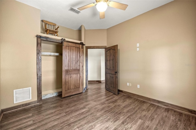 unfurnished bedroom with visible vents, a barn door, baseboards, and wood finished floors